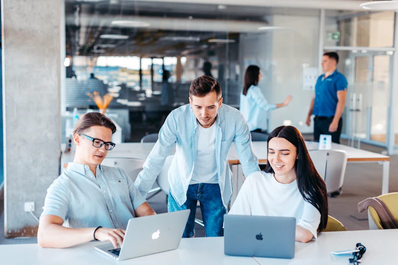 Drie collega’s werken samen aan laptops in een licht kantoor